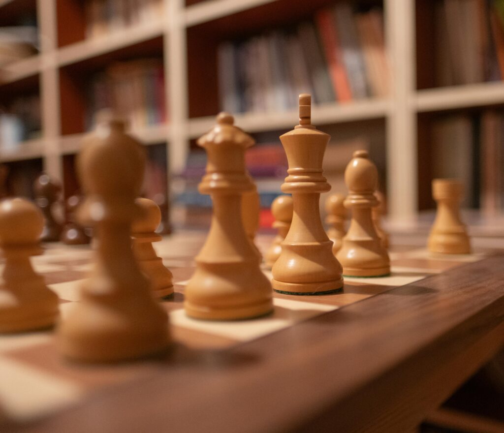 Close-up of wooden chess pieces on a chessboard in a warm, cozy library setting.